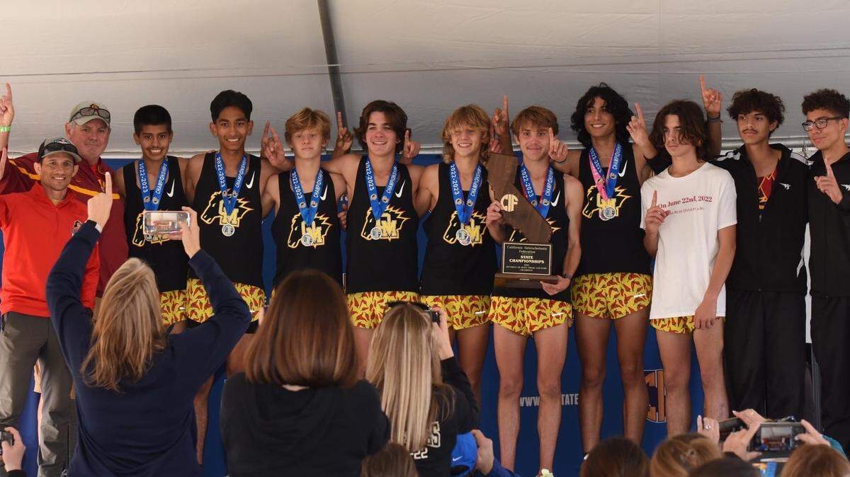 Oakdale cross country runner pose with head coach Guy Fowler and assistant coach Vic Moreno after winning the Division III State Championship at Woodward Park in Fresno on Saturday, Nov. 26, 2022.