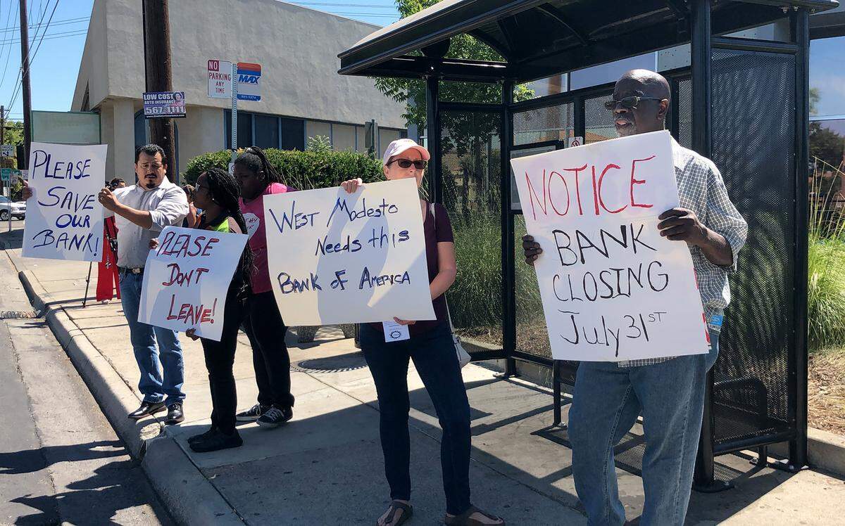 Ron DeLoach (right) and Linda Duran (center) protest the bank closure with others in front of Bank of America on Paradise Road in Modesto, Calif.