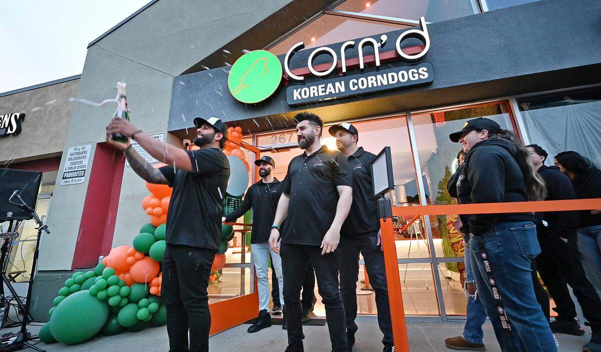 Co-owner Romeo Esho, left, uncorks a bottle of sparkling wine with his business partners during the grand opening of Corn’d Korean corn dogs in Turlock, Calif., Tuesday, Feb. 13, 2024.