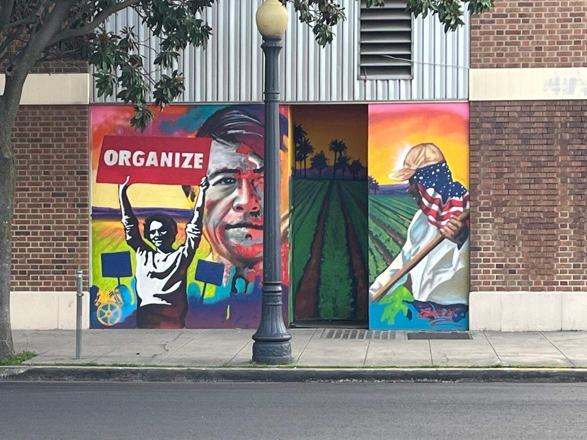 A mural shows and image of Cesar Chavez with Delores Huerta holding a sign that reads "Organize!" and a farm worker in a field 