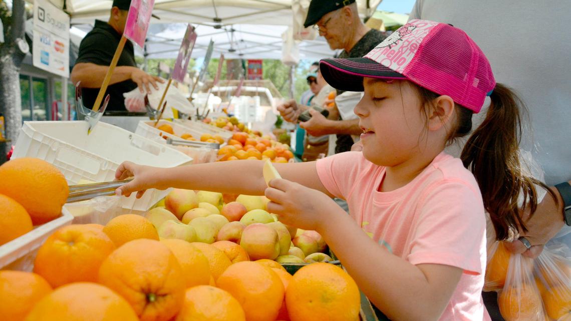 Coraline Estrada, 6, reaches for an apple slice at the Turlock Certified Farmers Market on its opening day and return to Main Street in downtown Turlock, Calif. May 4, 2019.