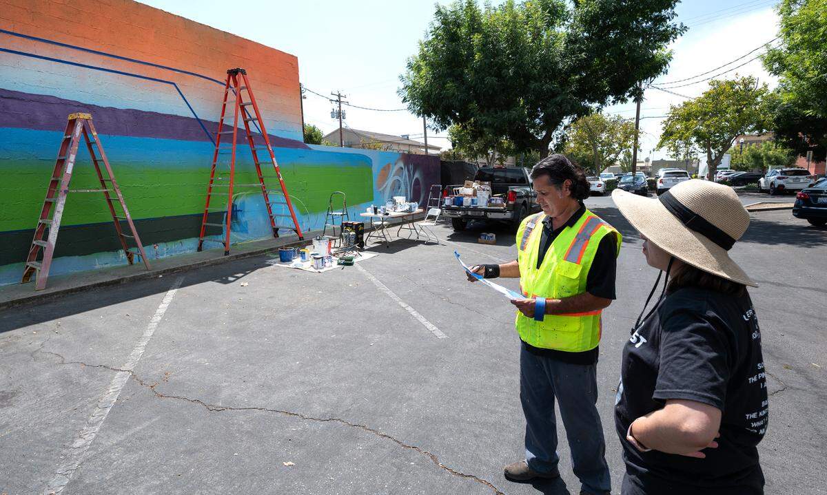 Artist Richard Gomez works from a drawing as he and Perla Serna, right, work on the mural “Chicano Downtown,” in Turlock, Calif., Saturday, September 9, 2023. Turlock West Side Story Mural Project is funded with a grant from the Heartland Creative Corps and the Carnegie Art Center.