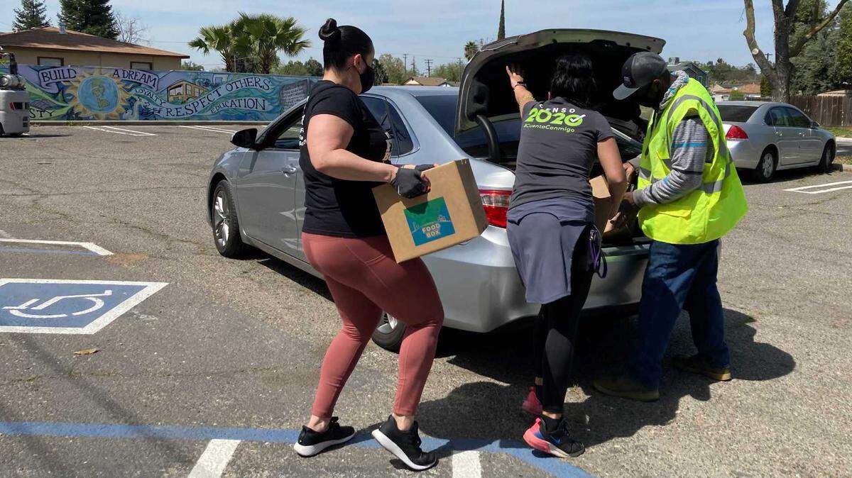 Volunteers load a vehicle with a box of food during the West Modesto Collaborative drive-thru giveway in Modesto, California, on Friday, April 2, 2021.