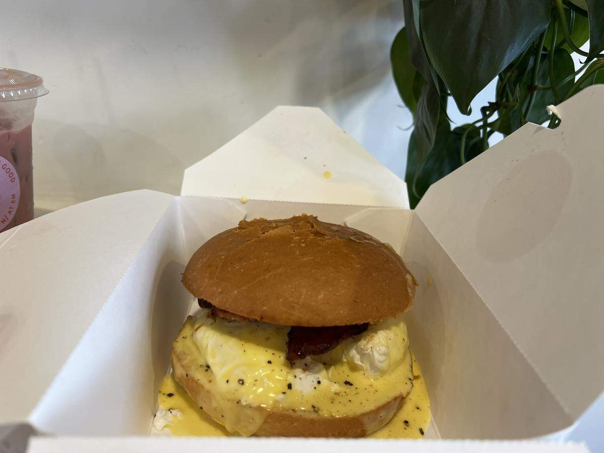 The Benny on a Bun from the Lucille breakfast menu, which is a brioche bun topped with white cheddar, bacon, cracked pepper, poached eggs and hollandaise sauce, priced at $12.50.