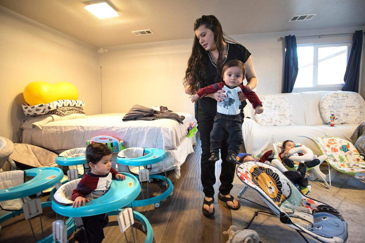 Tania Villanueva carries with their 1-year-old Julian as she puts them into walkers at their home east of Hughson, Calif., on Thursday, Dec. 16, 2021. Tania gave birth to the quadruplet brothers on New Year’s Eve of 2020.