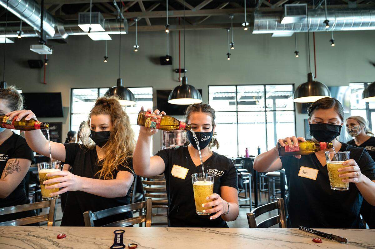 From the left, servers Rachael Falke, Lauryn Bairos, and Jess Miller practice pouring bottled beer during training at The Brass Tap restuarant in Modesto, Calif., on Friday, April 23, 2021.