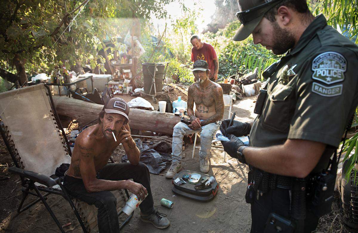 Modesto park ranger Justin Rocha, right, informs Alan Sanchez, left, of a 72-hour notice to vacate his campsite in Tuolumne Regional Park in Modesto, Calif., on Friday, September 9, 2022.
