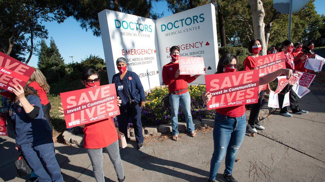 Hospital nurses hold signs calling for more personal protective equipment in front of Doctors Medical Center in Modesto, Calif., on Wednesday, August 5, 2020.