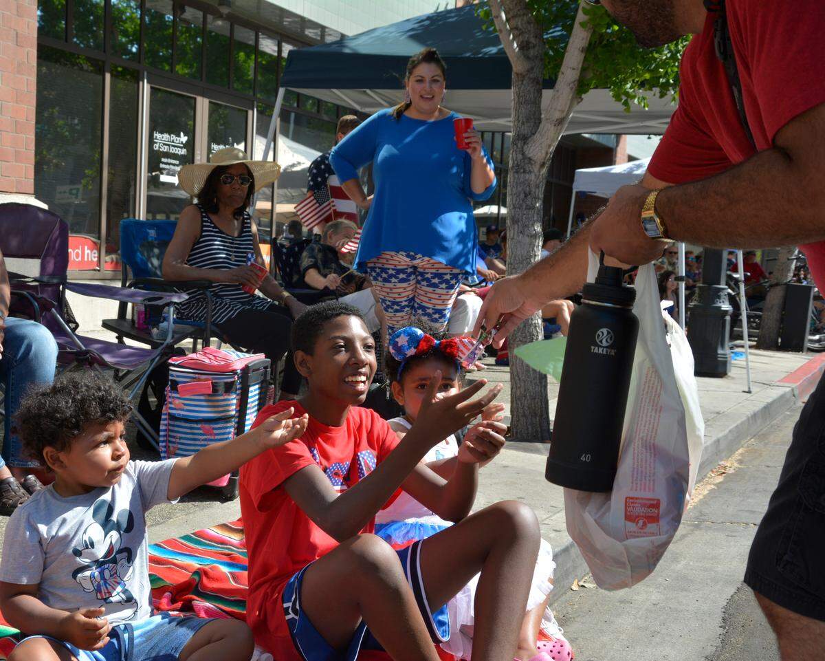 Twelve-year-old Triston Allen (center) gets candy from a participant in the Modesto Independence Day Parade while cousins Fletcher Allen (left) and Ruby Allen look on July 3, 2021 in Modesto, CA.