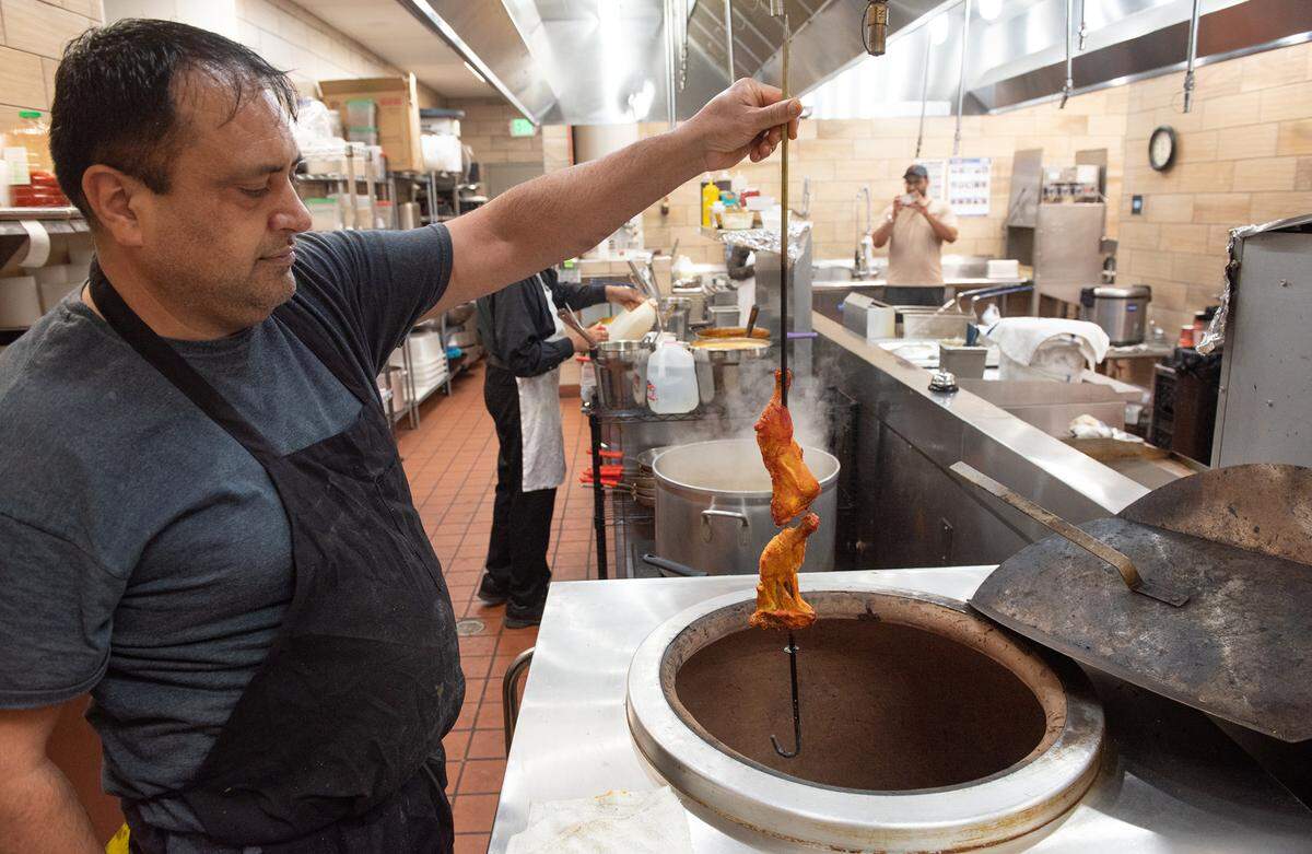 Cook Raj Singh shows the chicken in the tandoor clay oven at Tandoori Flame restaurant in Patterson, Calif., on Friday, April 22, 2022.