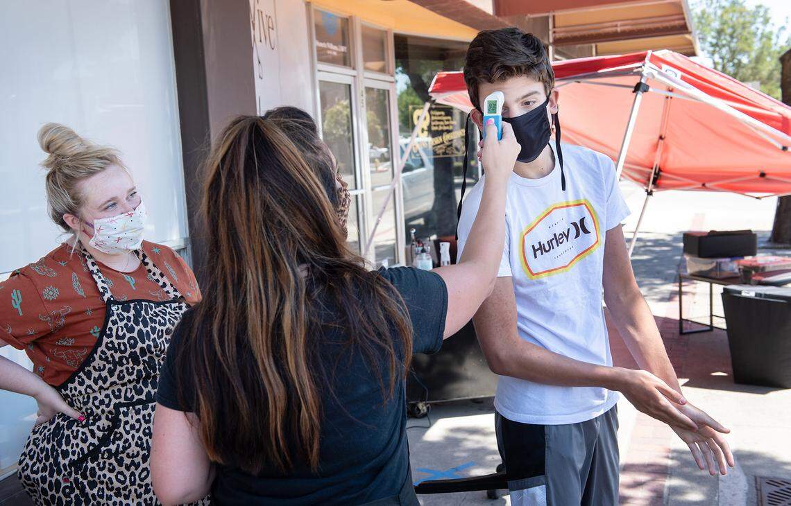 Revive Salon owner Jaqueline Wilson tests Kyle NeVille, 15, before a haircut on the sidewalk outside in Oakdale, Calif., on Saturday, August 1, 2020.