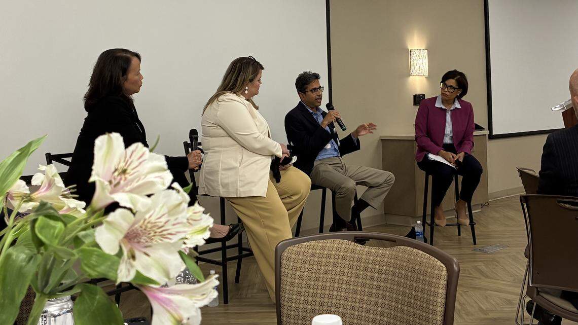 A man holds a microphone and speaks while two other panelists and the moderator look on.