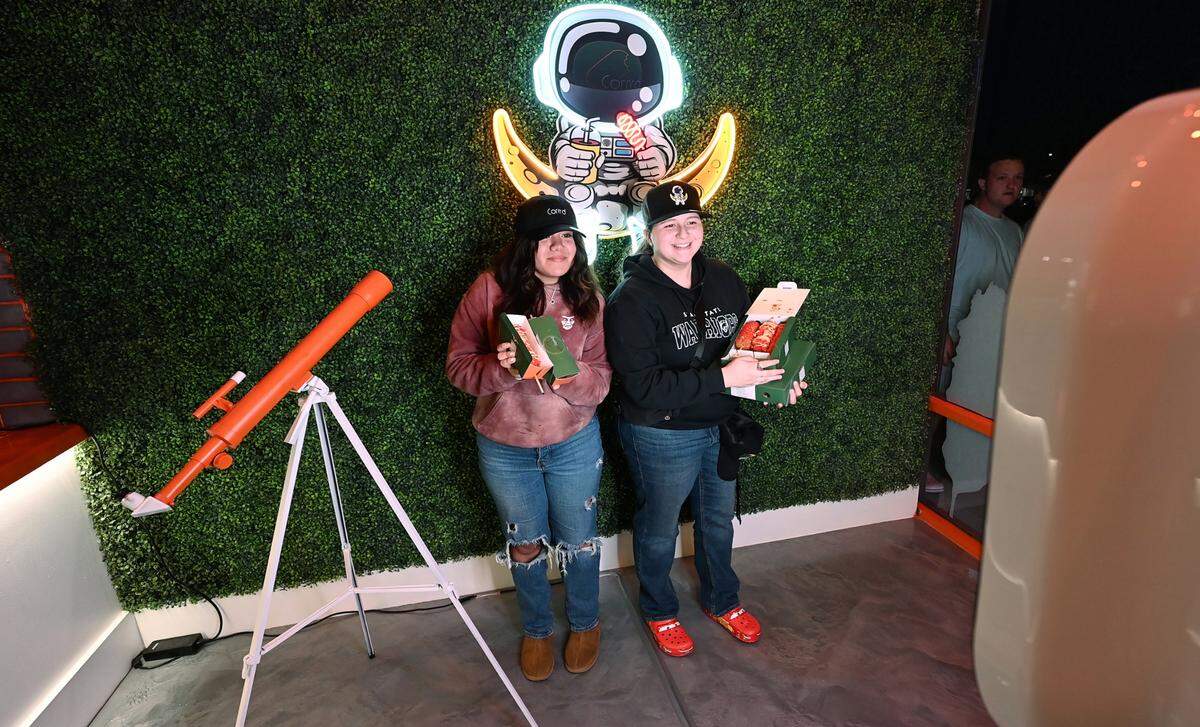 Perla Perez, left, and Amanda Alfaro, right, take a selfie with their corn dog haul during the grand opening of Corn’d Korean corn dogs in Turlock, Calif., Tuesday, Feb. 13, 2024.