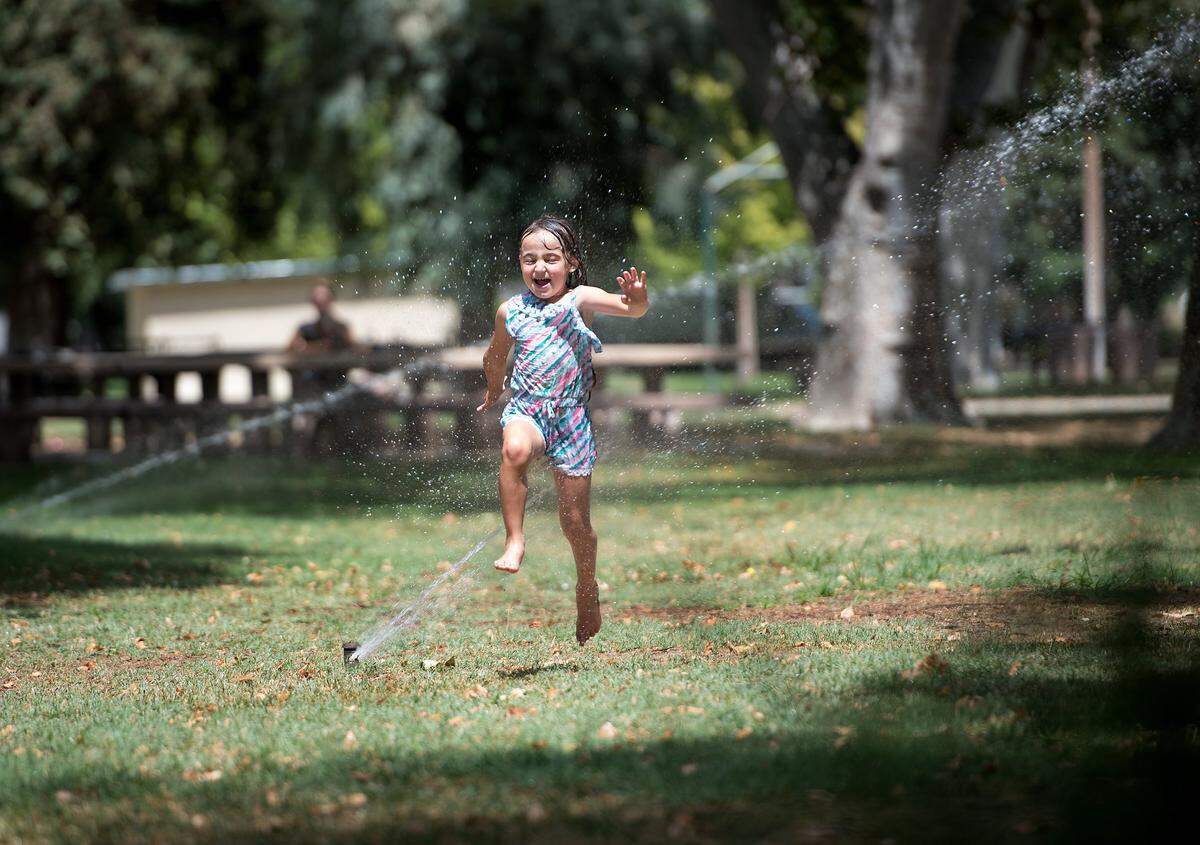 Marina Gutierrez, 5, runs through the sprinklers at Crane Park as her mother watches in Turlock, Calif., Friday, July 13, 2018. 