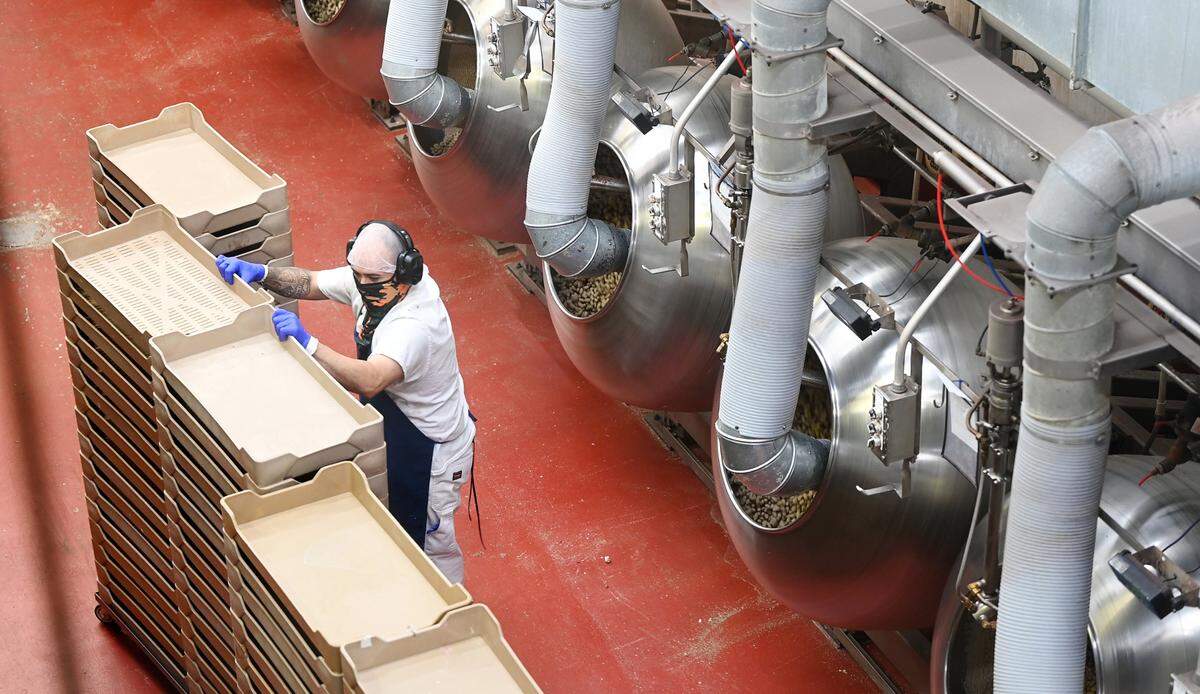 A worker arranges trays as candy is coated in large cans at Sconza Chocolates in Oakdale, Calif., Thursday, May 30, 2024.