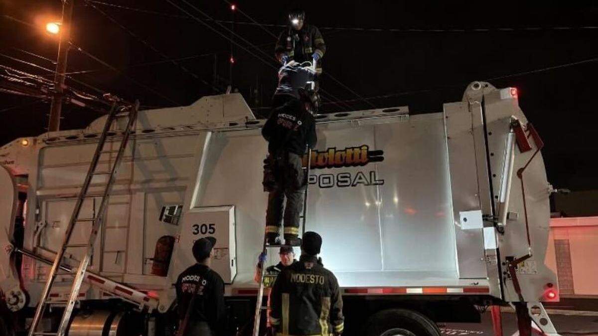 Modesto firefighters assist a man out of a garbage truck early Monday near 12th and I streets. Officials said the man had been inside a garbage bin when it was emptied into the truck.