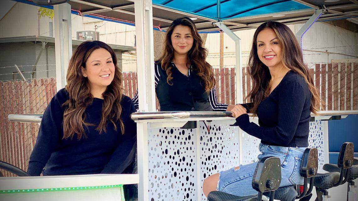 Central Valley Party Bikes owner Noel Dickey (left) poses for a picture on a 15-seat bicycle with Yelena Tsymbal, owner of Loza Wine & Crepes, and Sonia Grove, owner of SPG Extensions, in Turlock, Calif., on Oct. 18, 2021. The