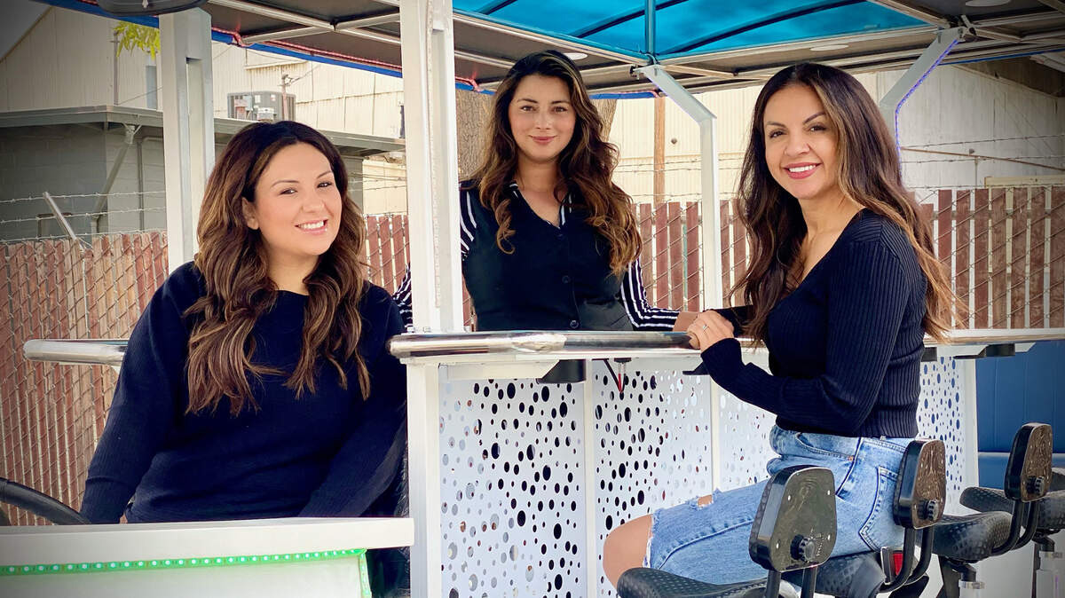 Central Valley Party Bikes owner Noel Dickey (left) poses for a picture on a 15-seat bicycle with Yelena Tsymbal, owner of Loza Wine & Crepes, and Sonia Grove, owner of SPG Extensions, in Turlock, Calif., on Oct. 18, 2021. The