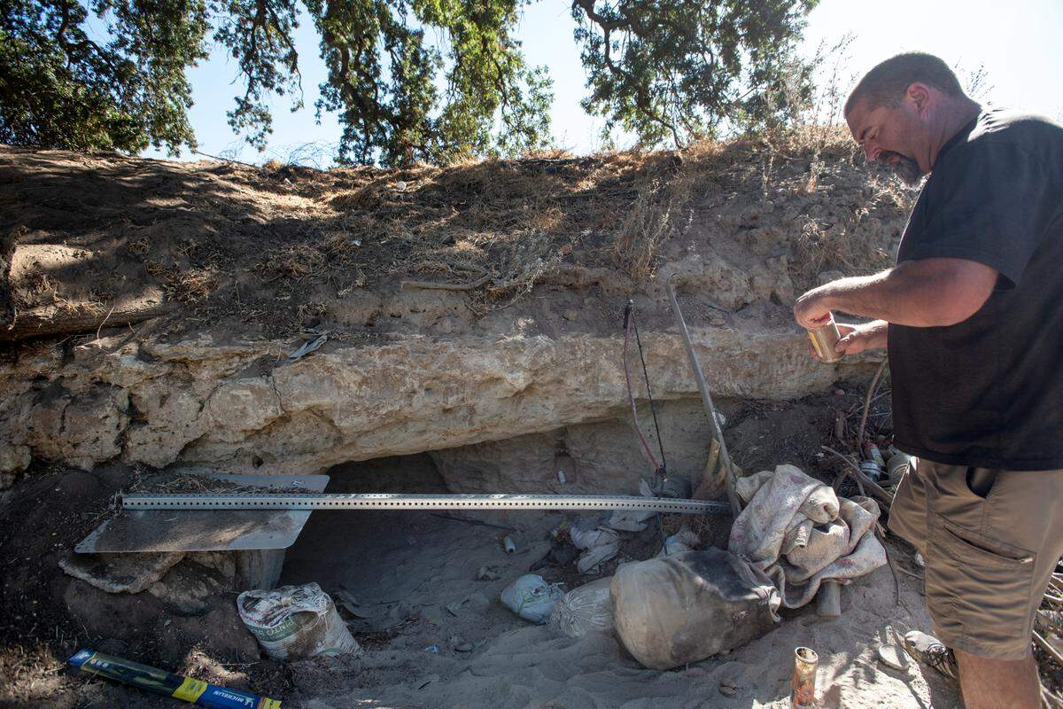 Chris Guptill looks through some discarded trash near a hand dug cave along the south side of the Tuolumne River near Crater Avenue in west Modesto, Calif., Thursday, Oct. 27, 2022.