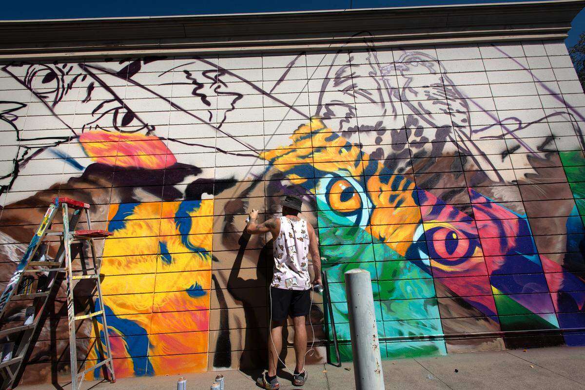 Muralist CAMER1sf works on a mural as part of the DoMo Walls Mural Festival in Modesto, Calif., in 2022.