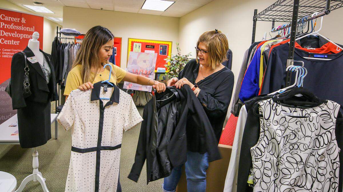Student assistant Yvonne Lee, left, and Rebecca Stephens, recruitment and career specialist, handle donated clothing at the Warrior Wardrobe at California State University, Stanislaus, in September 2019. Warrior Wardrobe provides free business attire for cash-strapped students preparing for job interviews.