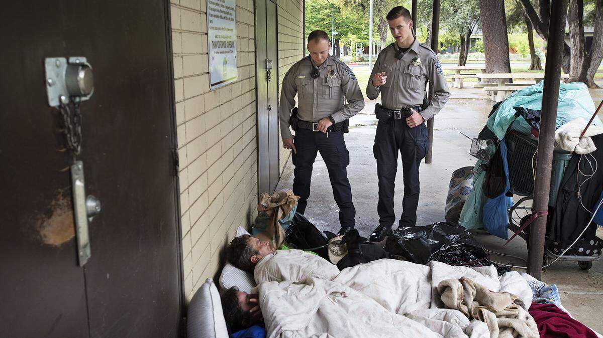 Modesto Police Department cadets Steven DiGiorno, left, and Jared Halderman, right, wake a homeless couple at Graceada Park in Modesto, Calif., on Tuesday, April 18, 2017.