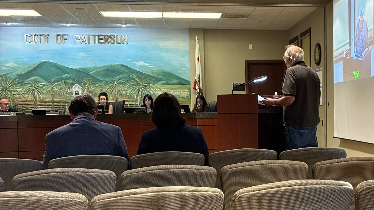 An older man stands at a podium speaking towards members of the Patterson city council