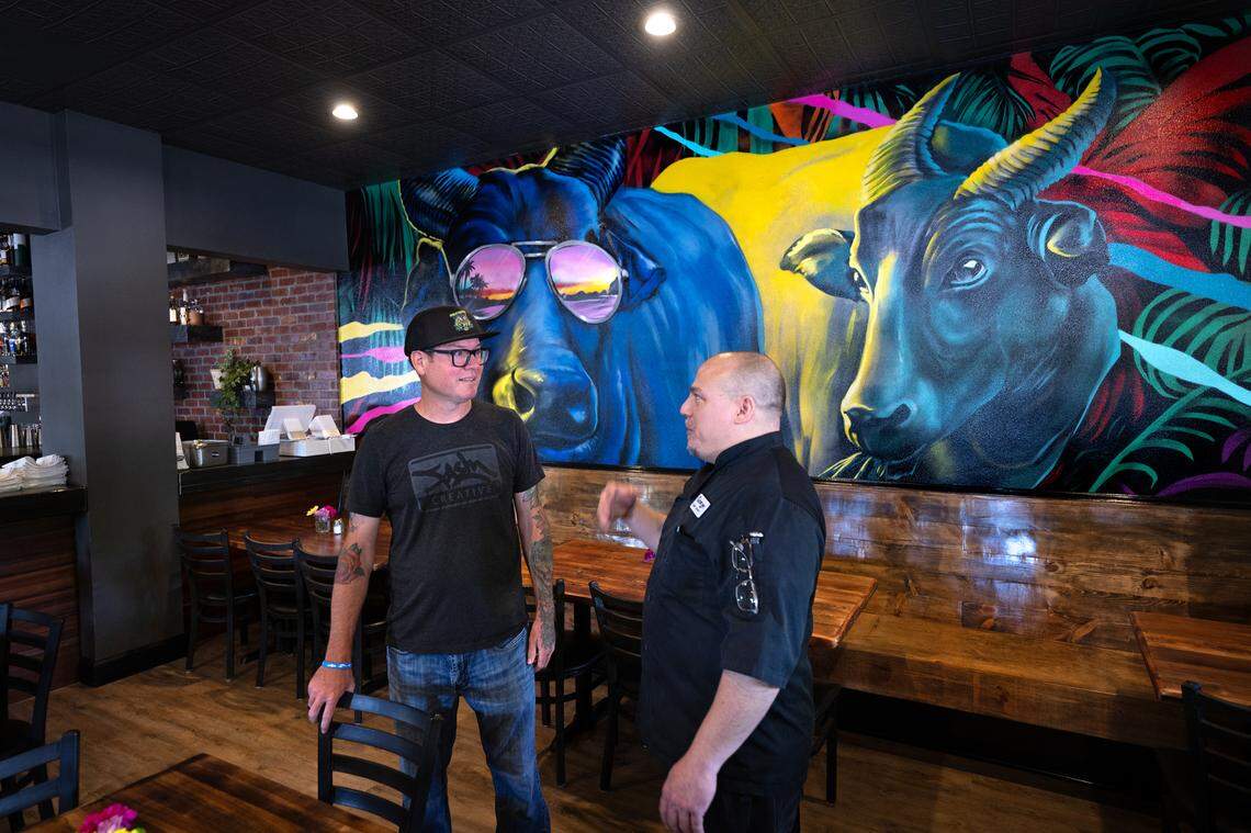 Owner and chef George Bertaina talks with artist FASM, aka Aaron Vickery, at Cora restaurant in Roseburg Square in Modesto, Calif., Friday, May 24, 2024. FASM painted the mural on the dining room wall.