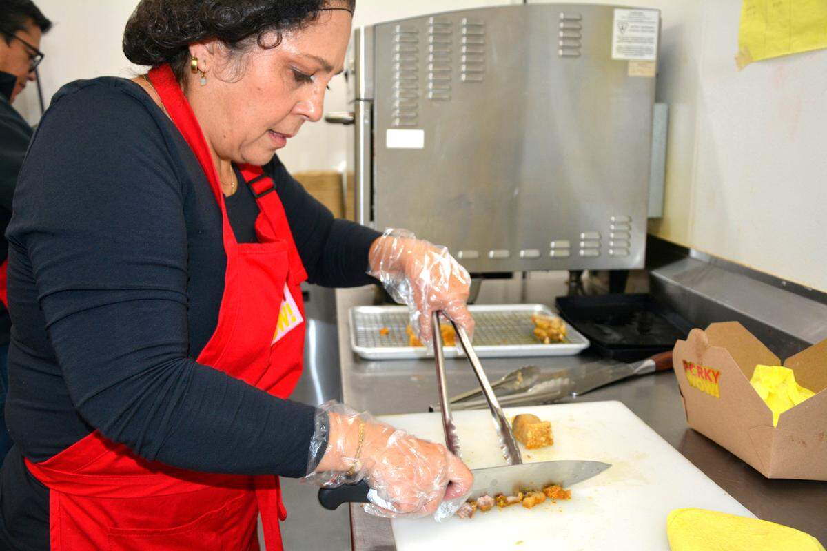 Maggy Bernal, wife of Porky Wow owner Fabricio Bernal, cuts chicharrones for tacos in Turlock, Calif. Nov. 16, 2022.