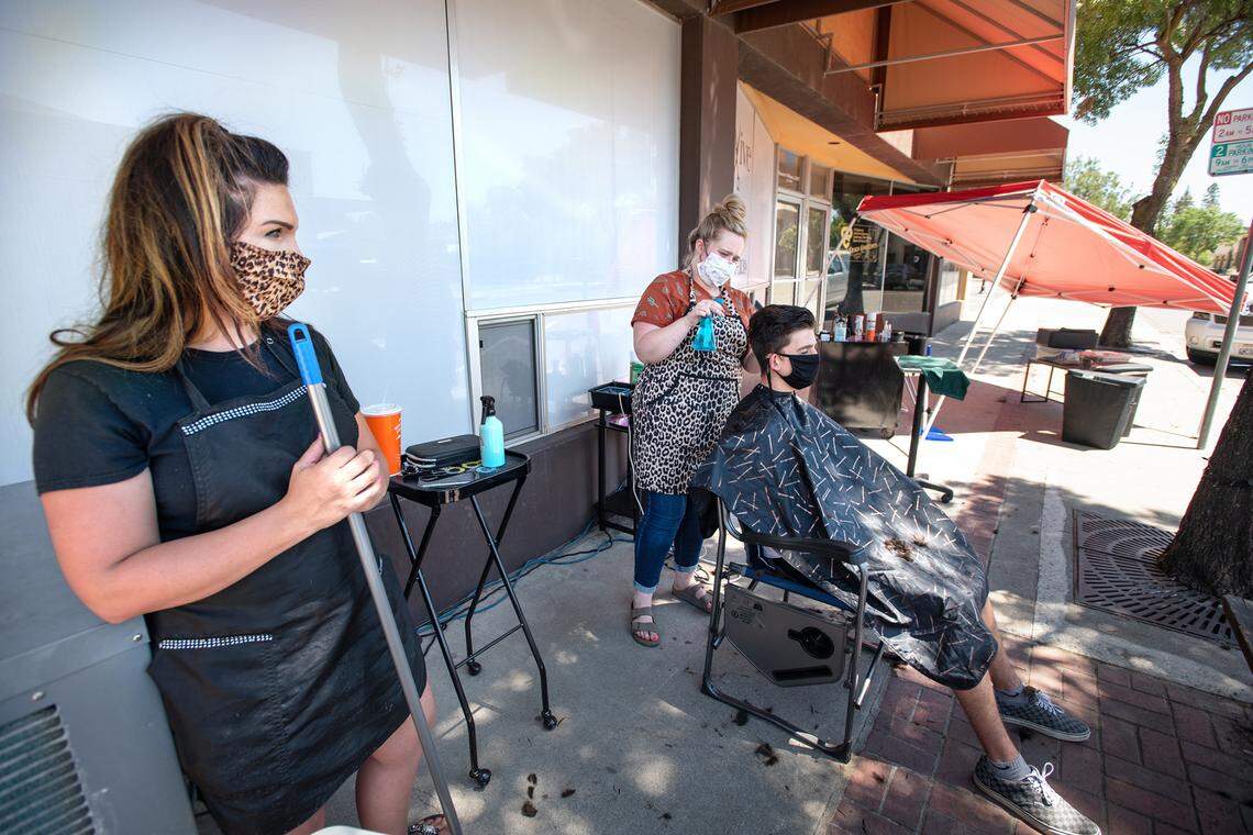 Revive Salon owner Jackie Wilson, left, has opened her salon for haircuts on the sidewalk outside in Oakdale, Calif., on Saturday, August 1, 2020.
