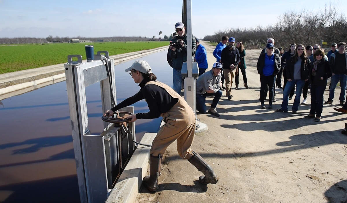 Almond farmer Christine Gemperle opens a gate to flood her orchard as part of a TID groundwater recharge program near Keyes, Calif., Wednesday, Jan. 18, 2023. The Turlock Irrigation District launched the recharge project in the fall with Sustainable Conservation, a nonprofit based in San Francisco, and the California Department of Water Resources.