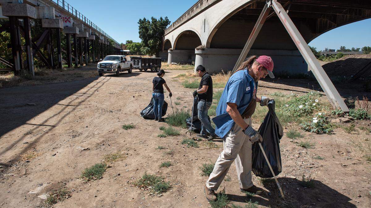 Volunteers Scott Jacobs, right, Bryan Guardado and Arianna Ansari, middle, pick up trash and other garbage during the Operation 9-2-99 clean-up at Gateway Park in Modesto, Calif., on Saturday, July 16, 2022.