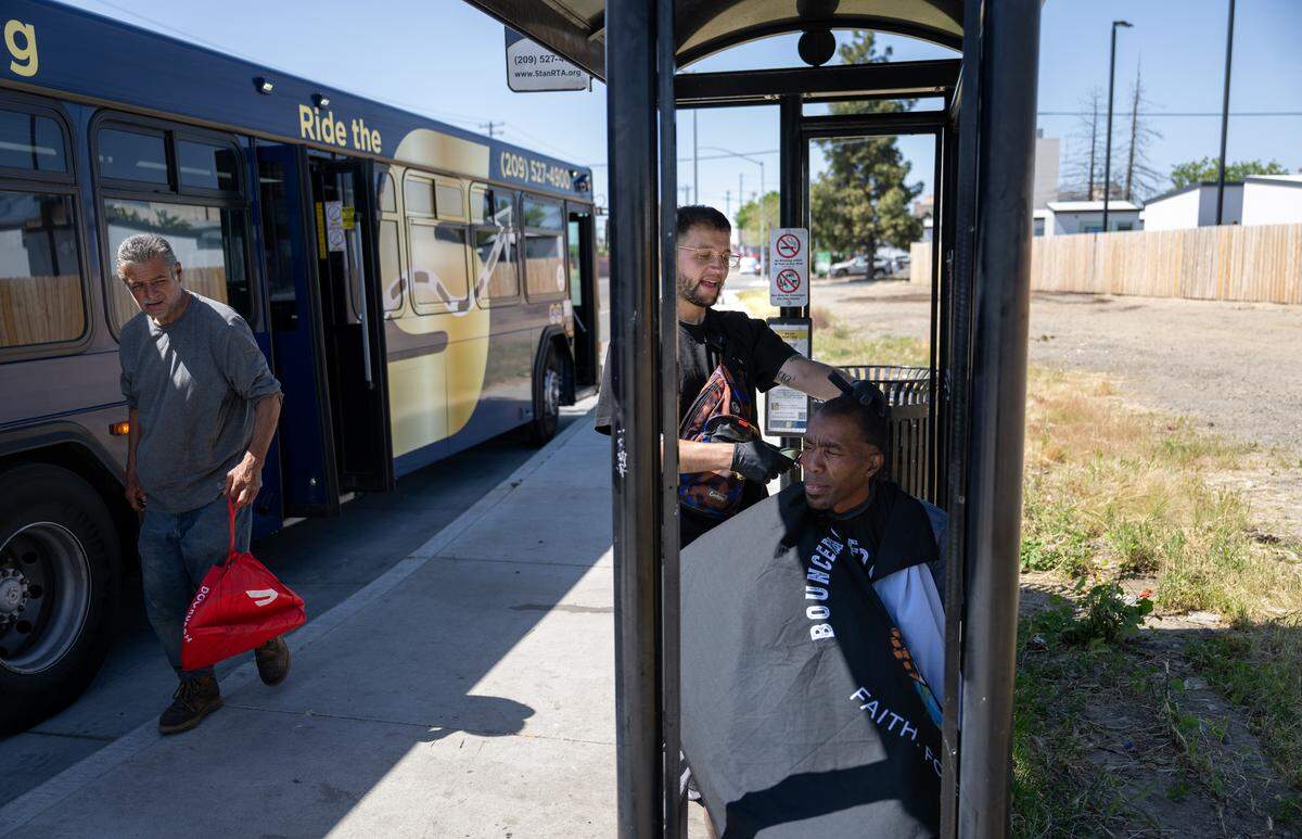 Paul Samsin, aka Sammy, cuts the hair of Johnny Ray at a bus stop on Ninth Street in Modesto, Tuesday, April 8, 2025.