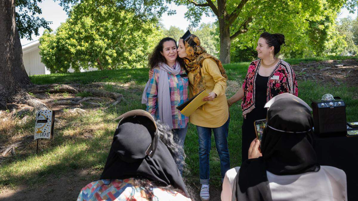 Estori Afzali, greets IRC business counselor Halima Mohammadi, left, and IRC senior education and health promoter Katharina Beeler, right, during a graduation ceremony at Davis Park in Modesto Calif., on Friday, July 1, 2022. Seventeen women refugees from Afghanistan are the first graduates of the International Rescue Committee and Modesto Junior College’s child care microenterprise development program for home child-care licensing.