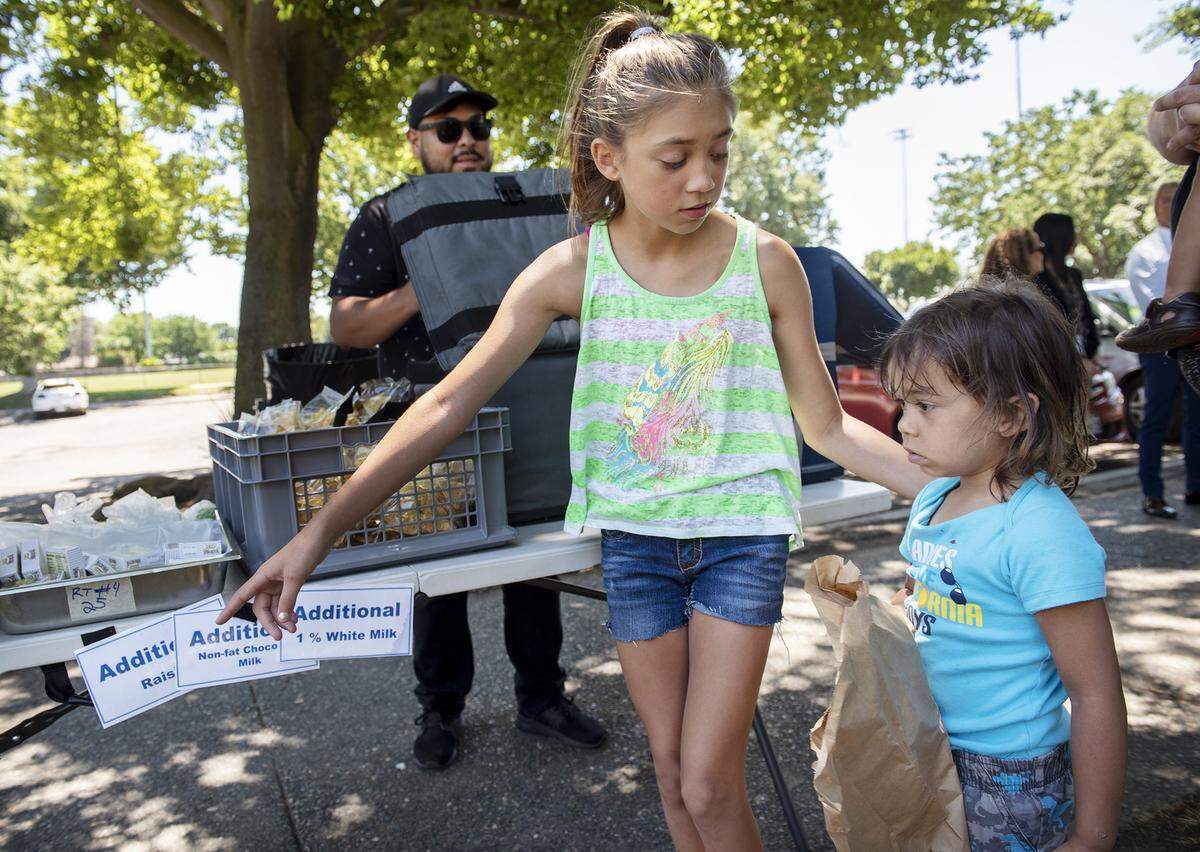 Rylee Aguliar, 11, helps her brother Austin, 4, with selecting lunch items at the Modesto City Schools summer lunch program in Downey Park in Modesto, Calif., Wednesday, June 19, 2019.