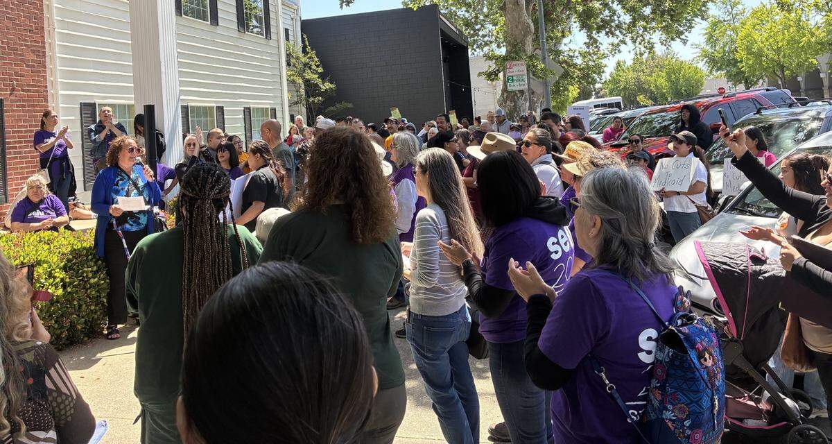A woman with a microphone speaks out to a large crowd outside of the building where Tom McClintock's office is. 