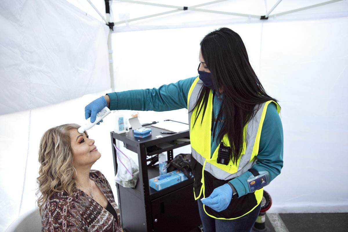 Safety Coordinator Janet Murillo test the body temp of employee Lisa Sanchez before entering the building at MTC Distributing in Salida, Calif., on Tuesday, April 14, 2020.