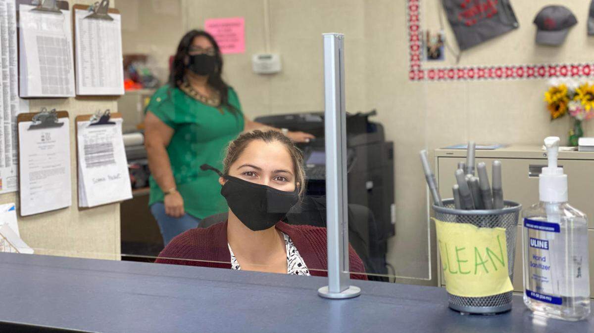 Secretaries Violeta Robledo and Liz Rodriguez are pictured in the office of Crowell Elementary School, where safety measures including plexiglass barriers, hand sanitizers and face coverings have been in place since staff returned to the campus to start distance learning this school year.