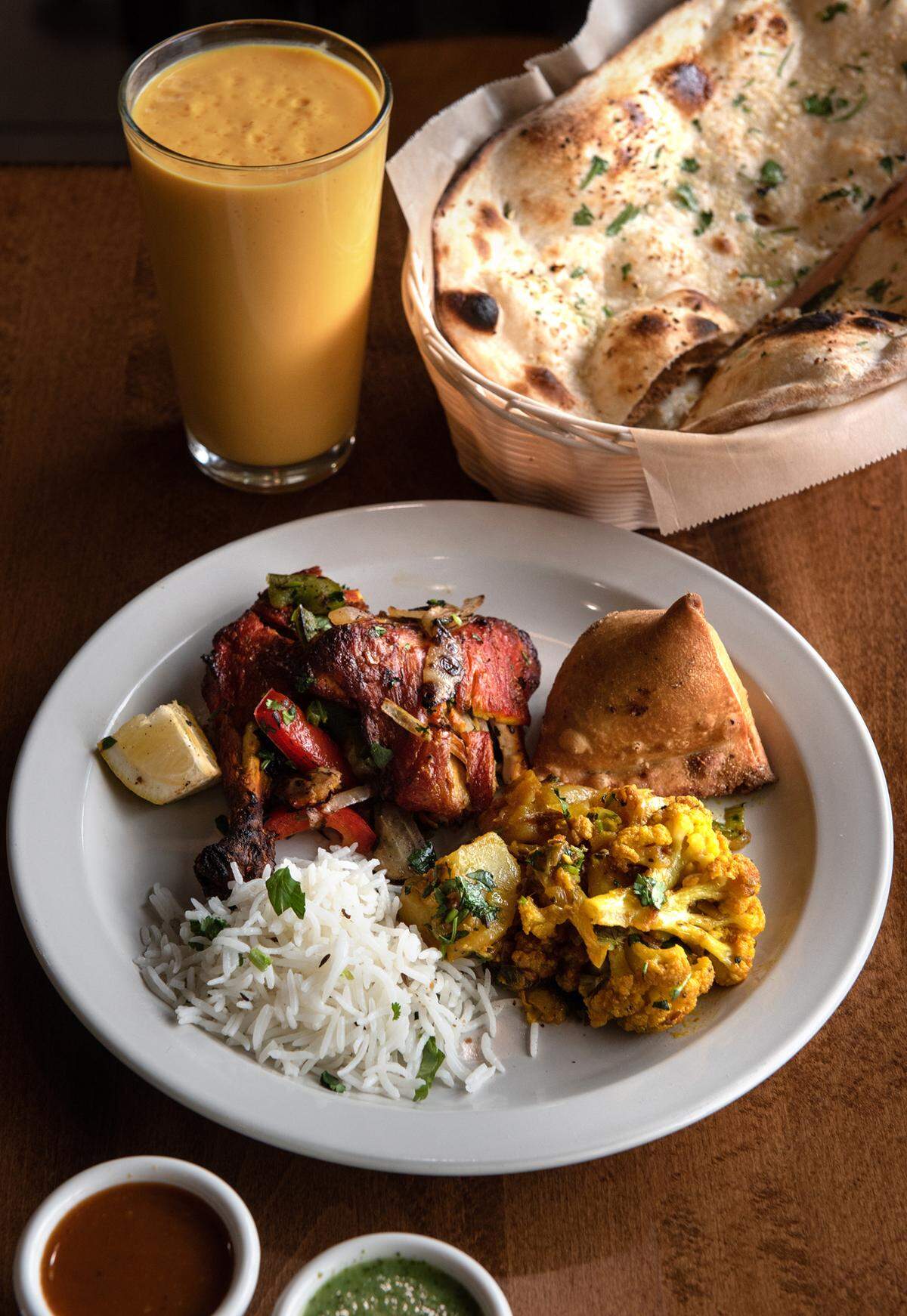 Tandoori chicken with house made vegetable samosa, Aloo Gobi (cauliflower and potatoes), mango lassi drink (mango and house made yogurt), rice and naan bread at Tandoori Flame restaurant in Patterson, Calif., on Friday, April 22, 2022.