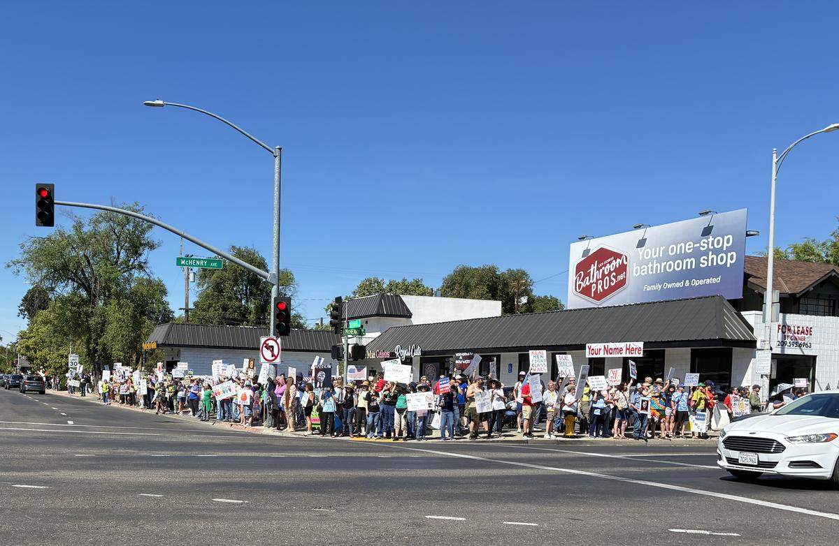 A crowd of people holing signs stand at the corner of McHenry and Needham St in Modesto.