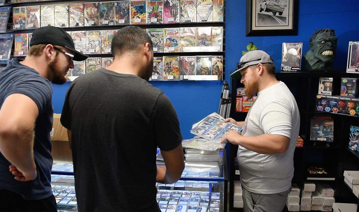 Owners Kyle Turner, right, shows Cameron Treciokas, left, and Frank Figueroa baseball cards at Turlock Comics in Turlock, Calif., on Wednesday, June, 15, 2022.