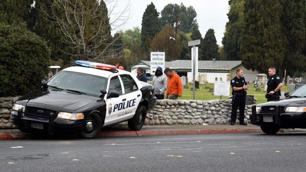 Officers with the Modesto Police department stand by as they wait for a tow truck to arrive to remove a cop car from the cemetery brick wall Wednesday (03-11-15) on Scenic drive near Bodem street in Modesto, Calif.