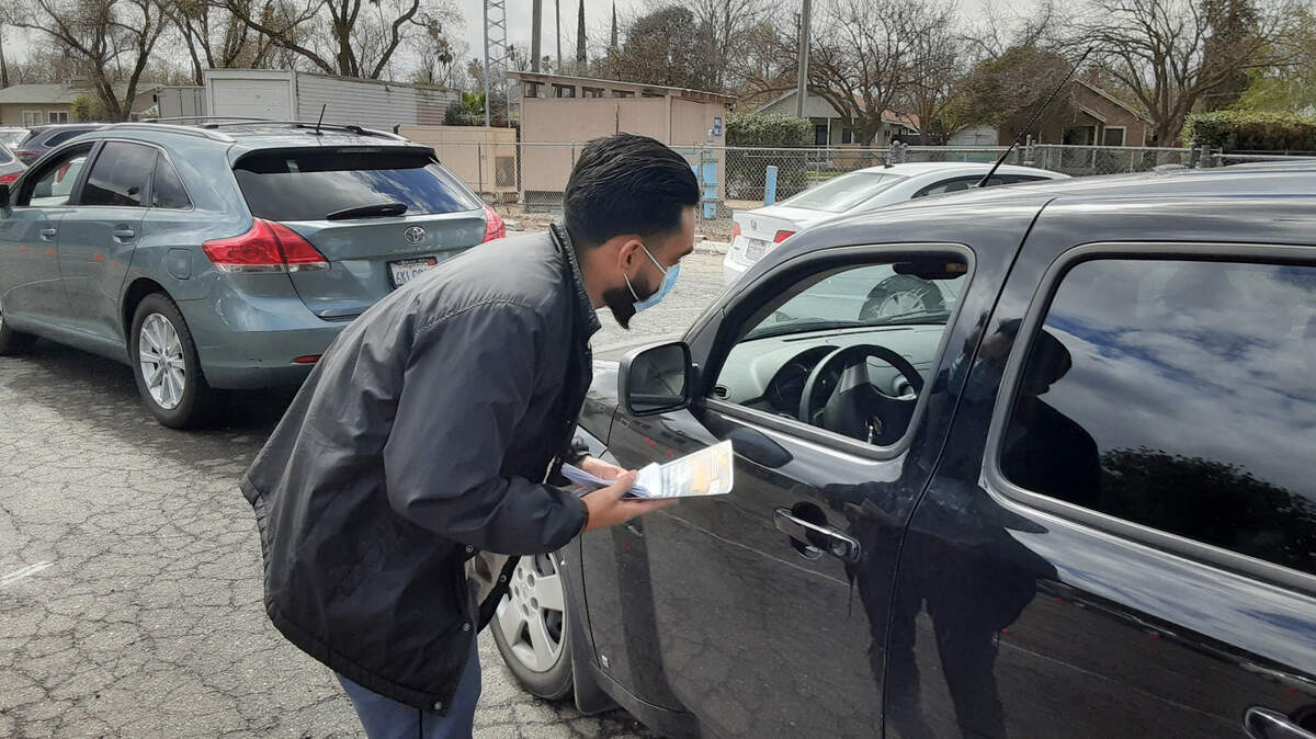 Mobile Outreach Assistance team member Nico Solorio speaks with a driver about the rental assistance program Monday, March 15, 2021, at The Gathering Covenant Church in Patterson, Calif. People were lined up for a food pantry giveaway.