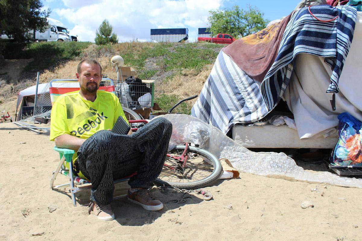 Terry Sump sits outside his tent in Turlock, Calif., on Tuesday, May 10, 2022. Another resident estimated about 55 people live in the encampment along Highway 99.