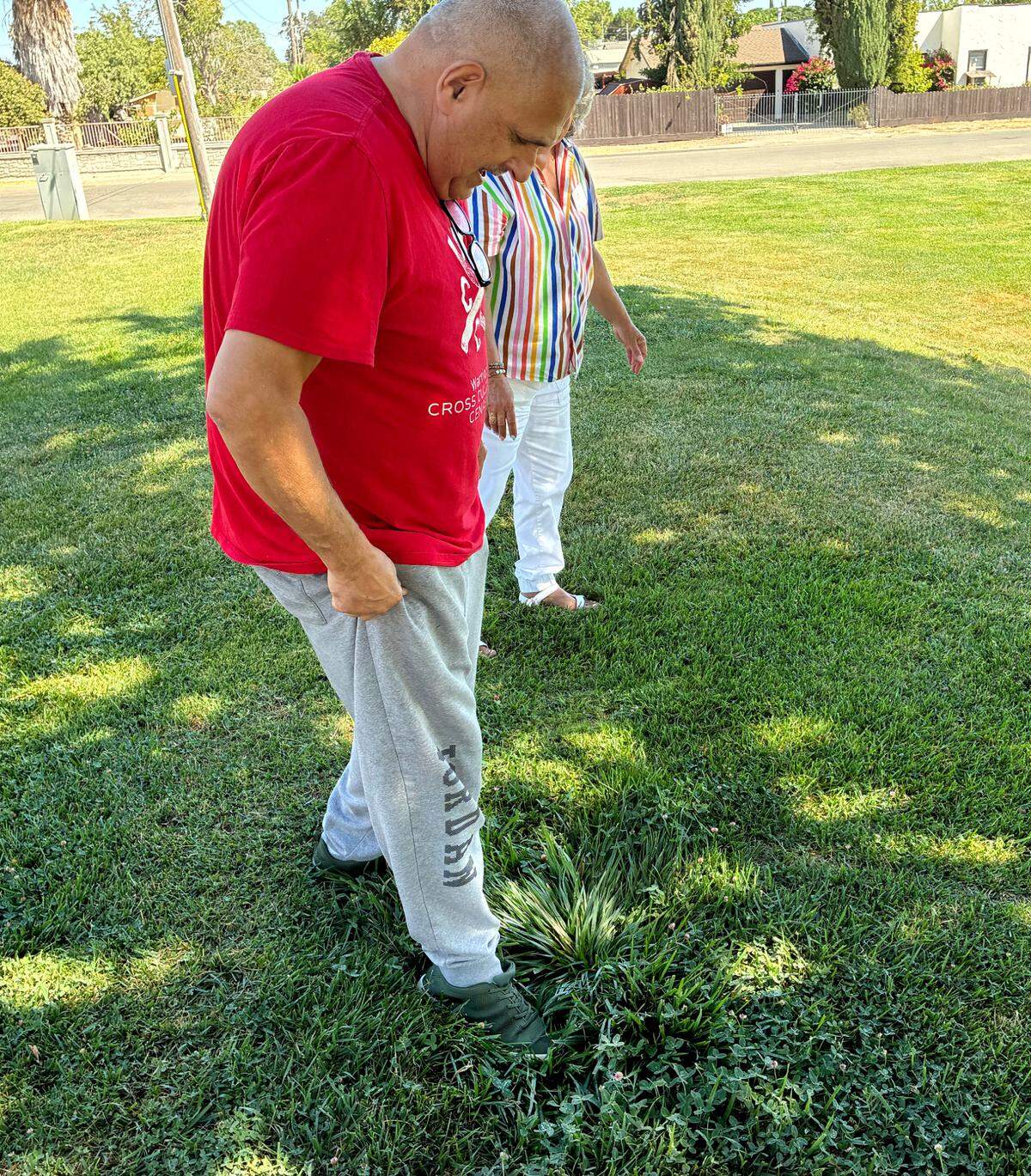 An older man puts his foot into a hole in the grass to show how deep it is. 