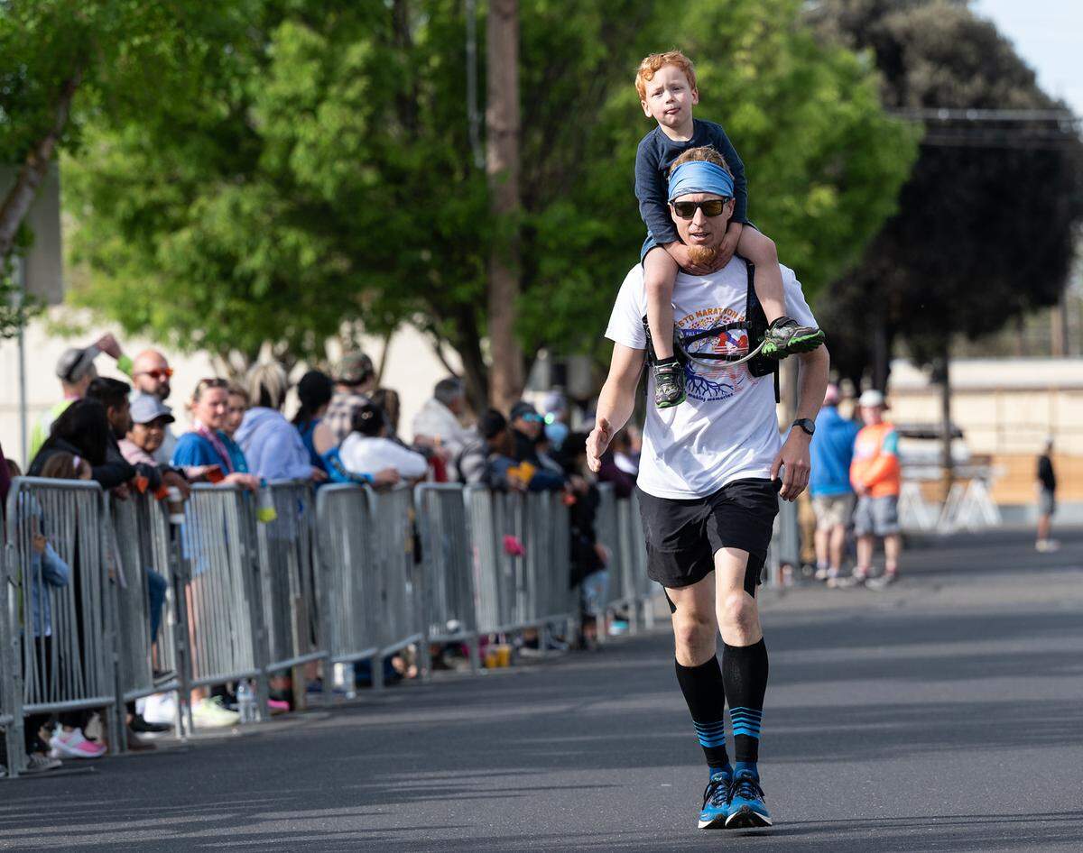 Drew Welch finishes the last block of the half marathon with his son Carson, 3, on his shoulders during the Modesto Marathon in Modesto, Calif., on Sunday, March 27, 2022.
