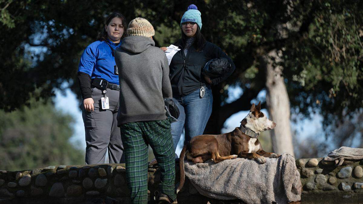 Community Health and Assistance Team (CHAT) outreach specialist Megan Dill, left, and BHRS housing specialist Asuzena Pena, right, talk with a homeless man in Tuolumne River Regional Park during Stanislaus County’s 2024 Point-in-Time count of unsheltered homeless people in Modesto, Calif., Thursday, Jan. 25, 2024.