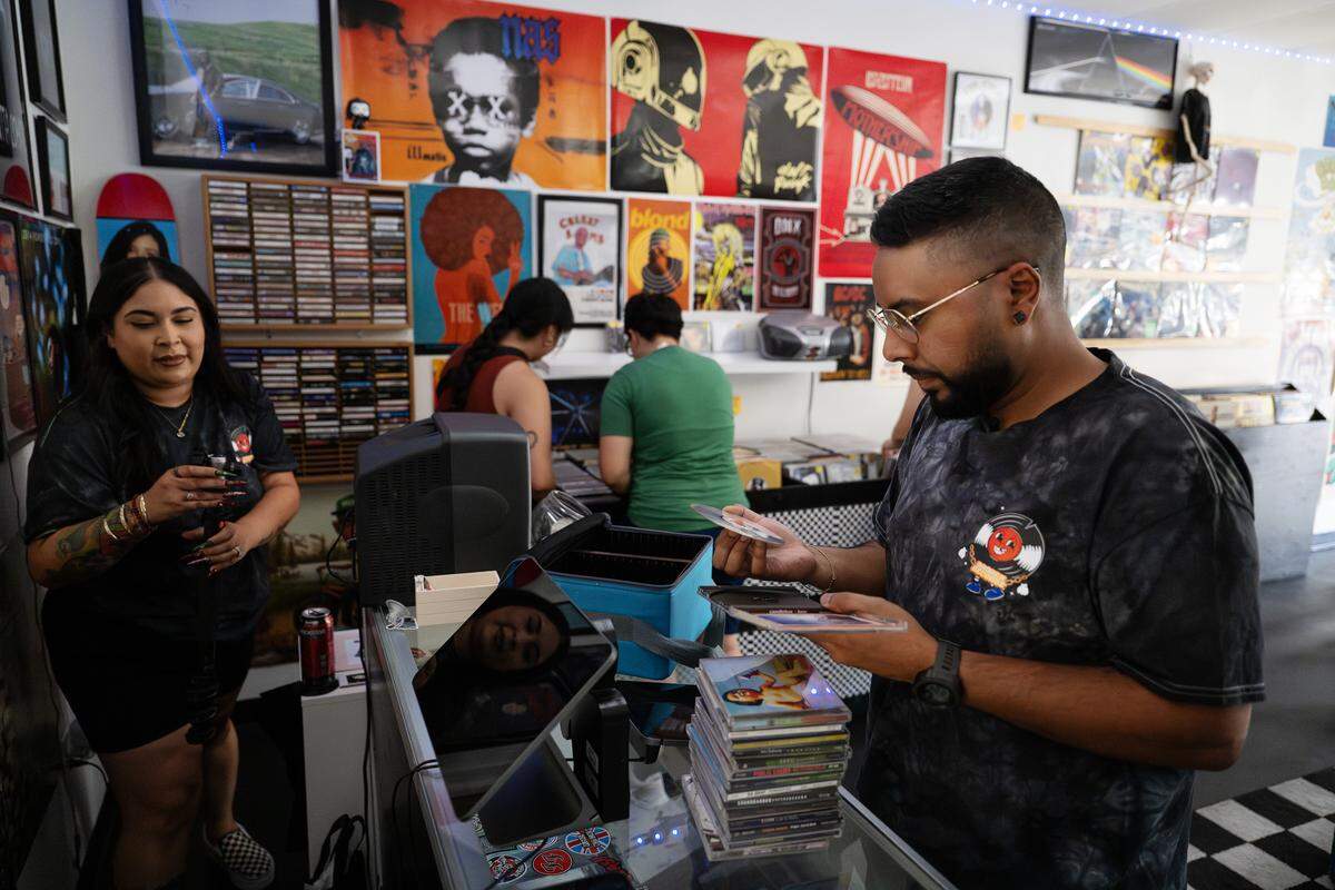 Broken Records co-owner Shavin Jit, right, looks over some compact discs that a customer brought in for trade in Modesto, Friday Aug. 22, 2025. The store also sells cassette tapes.