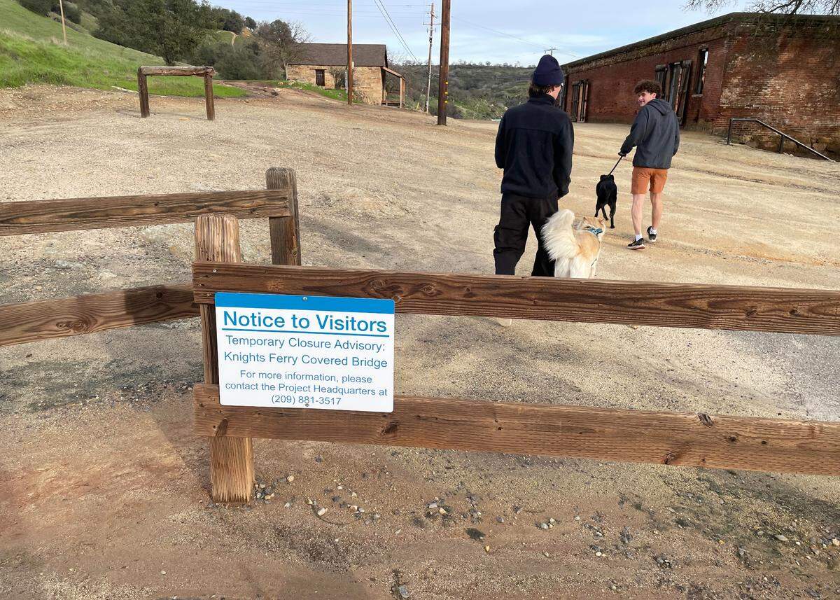 Visitors walk near signs announcing the temporary closure of the Knights Ferry Covered Bridge.