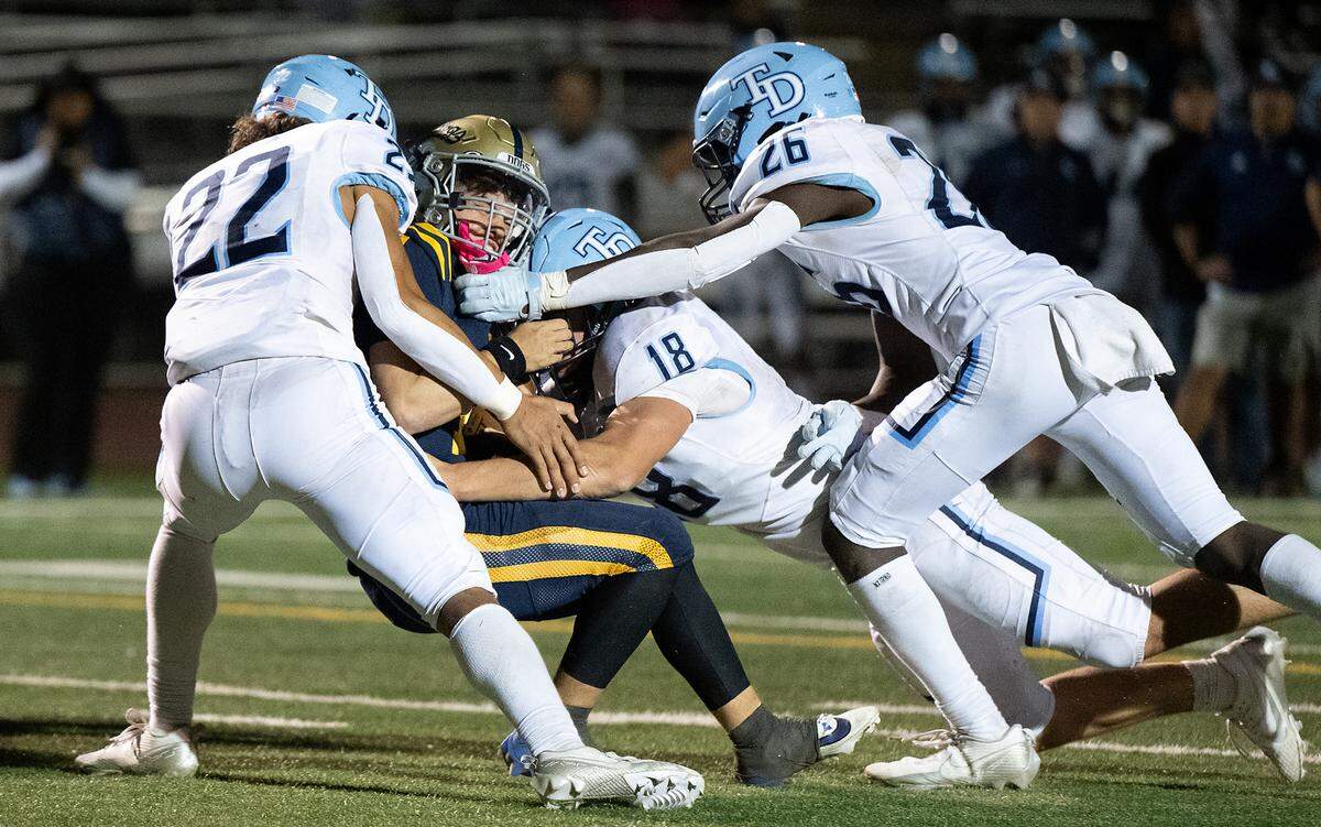 Downey’s Elias Haynes (22), John Hinchey (18) and Antwain Harper swarm Turlock quarterback Scout Silva during the Central California Athletic League game at Turlock High School in Turlock, Friday, Oct. 18, 2024.